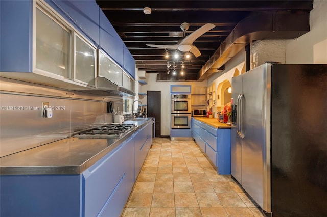 kitchen featuring wooden counters, beamed ceiling, stainless steel appliances, sink, and blue cabinetry