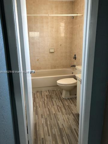 bathroom with tiled shower / bath, toilet, and wood-type flooring