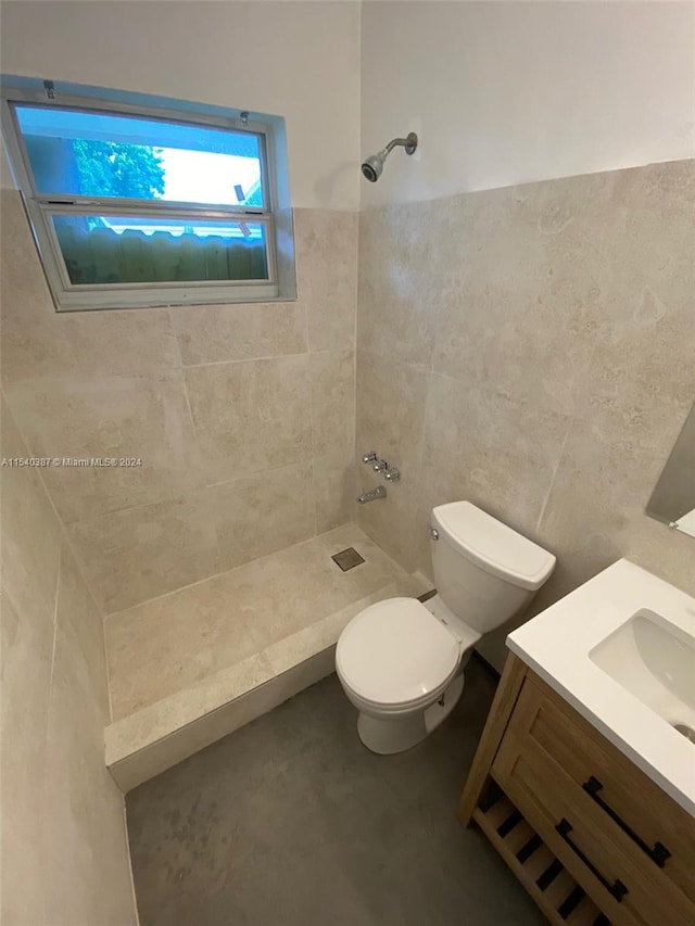 bathroom with tile walls, toilet, a tile shower, and vanity