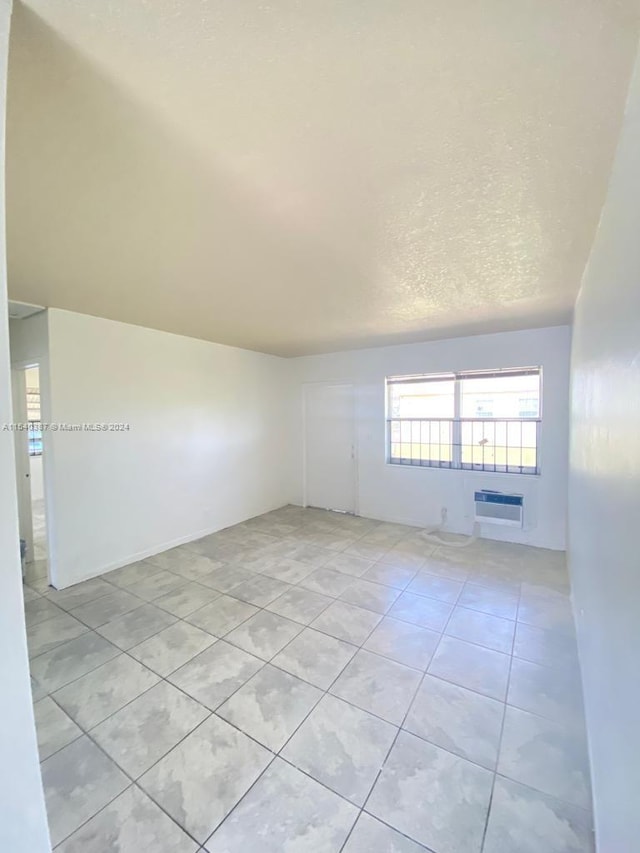 unfurnished room featuring a wall mounted air conditioner, a textured ceiling, and light tile flooring