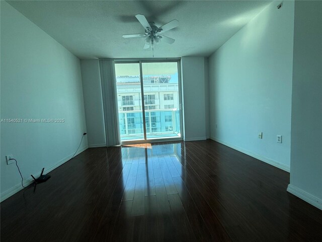 empty room featuring expansive windows, baseboards, a ceiling fan, and dark wood-style flooring