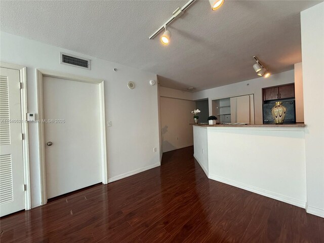 unfurnished living room with visible vents, a textured ceiling, baseboards, and wood finished floors
