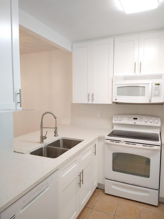 kitchen with light tile patterned floors, light stone countertops, sink, white cabinets, and white appliances