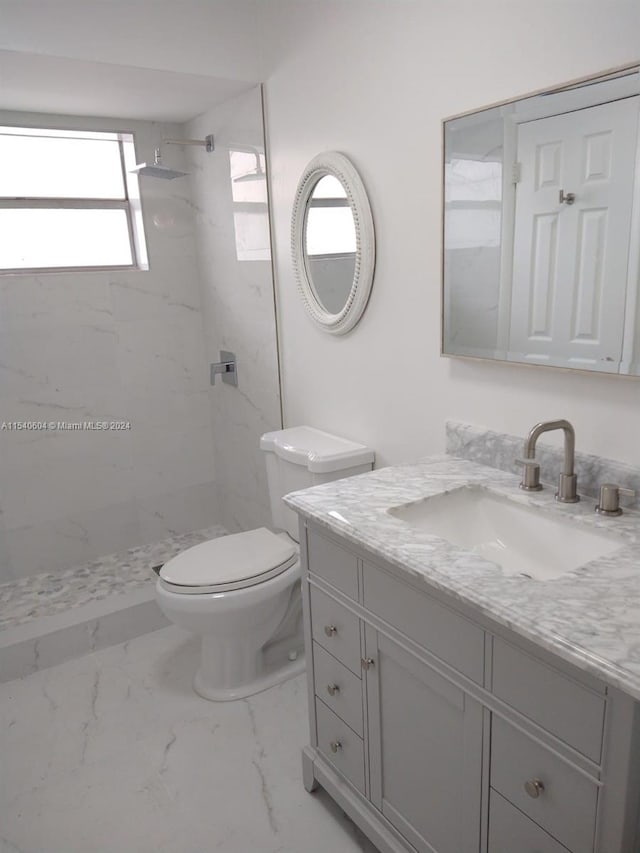 bathroom featuring a wealth of natural light, vanity, toilet, and a tile shower