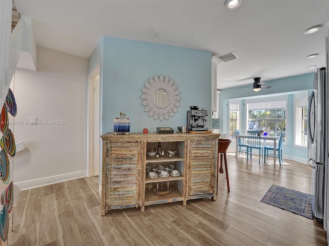 bar with ceiling fan, stainless steel refrigerator, and light wood-type flooring