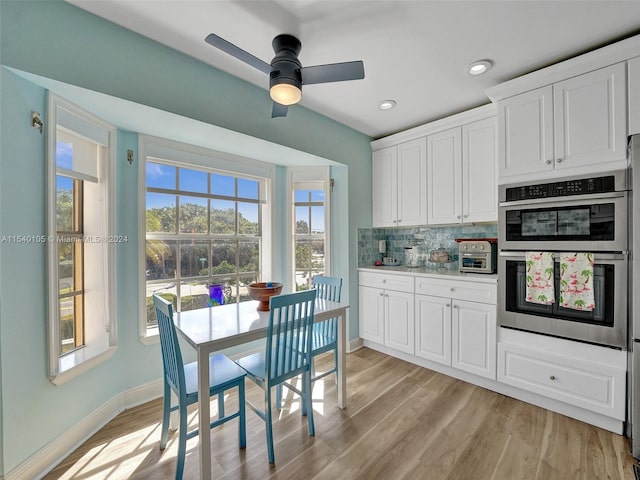 kitchen with stainless steel double oven, ceiling fan, light hardwood / wood-style flooring, white cabinets, and tasteful backsplash