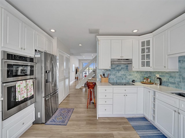 kitchen featuring white cabinets, light wood-type flooring, tasteful backsplash, and appliances with stainless steel finishes