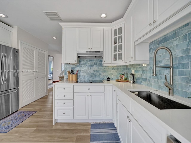 kitchen featuring sink, light hardwood / wood-style floors, stainless steel refrigerator, tasteful backsplash, and white cabinetry