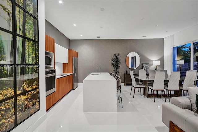 kitchen featuring stainless steel appliances, light tile floors, a kitchen breakfast bar, a kitchen island with sink, and sink