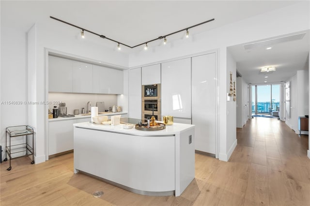 kitchen featuring a kitchen island, white cabinets, black microwave, and light wood-type flooring