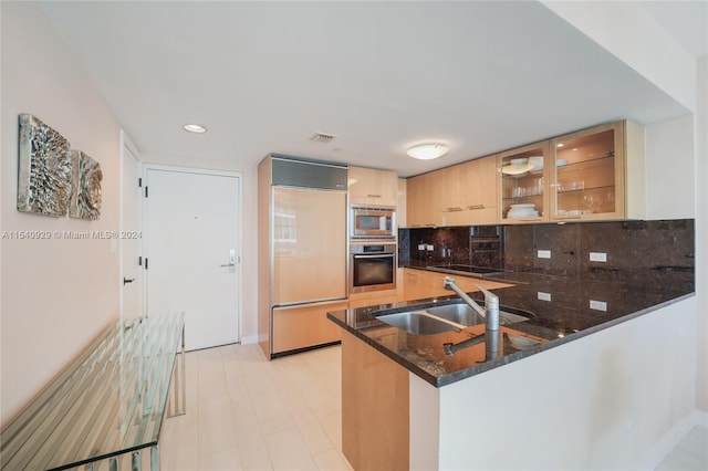 kitchen featuring built in appliances, kitchen peninsula, tasteful backsplash, dark stone countertops, and sink