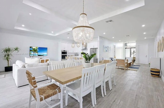 dining room featuring a tray ceiling, a chandelier, and light hardwood / wood-style flooring