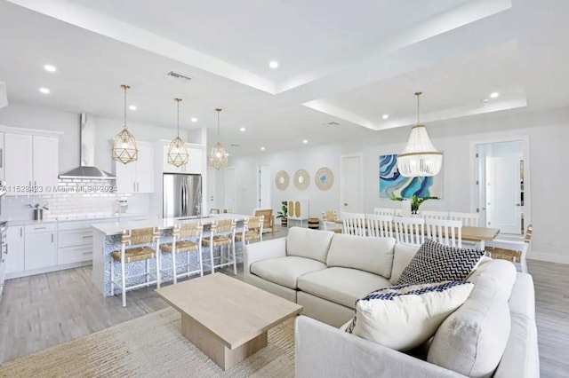 living room with a chandelier, a tray ceiling, and light hardwood / wood-style flooring