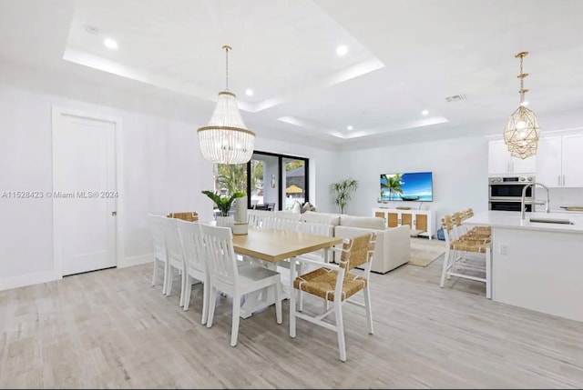 dining space featuring a raised ceiling, light hardwood / wood-style floors, a notable chandelier, and sink