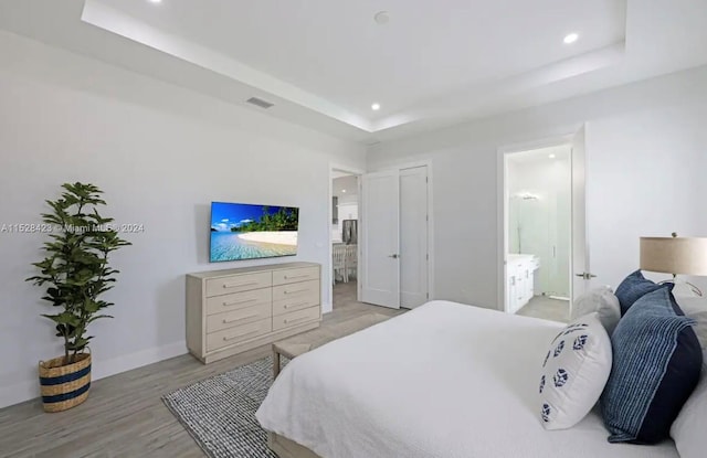 bedroom with a raised ceiling, ensuite bath, and light hardwood / wood-style flooring