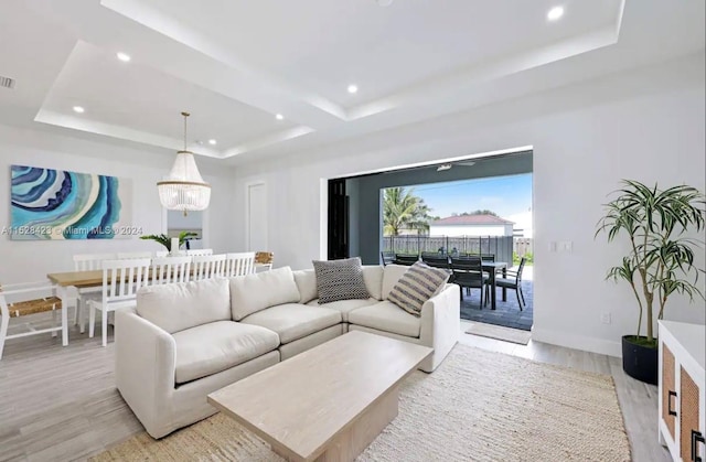 living room featuring a notable chandelier, a raised ceiling, and light wood-type flooring