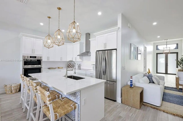 kitchen with white cabinetry, a kitchen island with sink, appliances with stainless steel finishes, light hardwood / wood-style flooring, and wall chimney exhaust hood