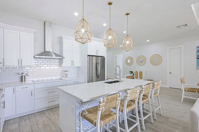 kitchen with pendant lighting, light hardwood / wood-style floors, wall chimney range hood, tasteful backsplash, and stainless steel fridge