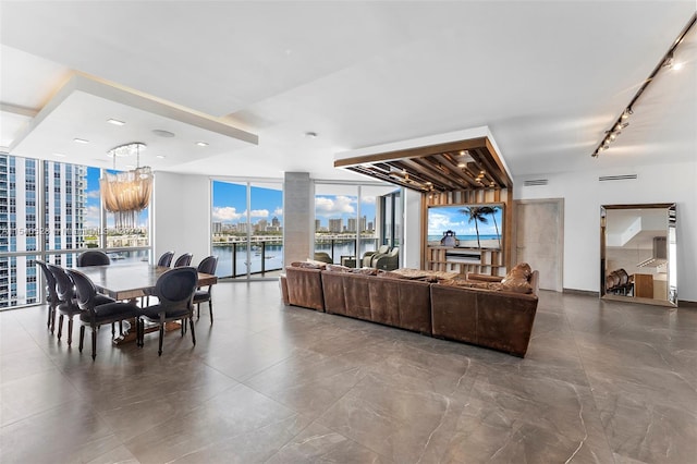 tiled living room featuring a water view, a wall of windows, track lighting, and a chandelier