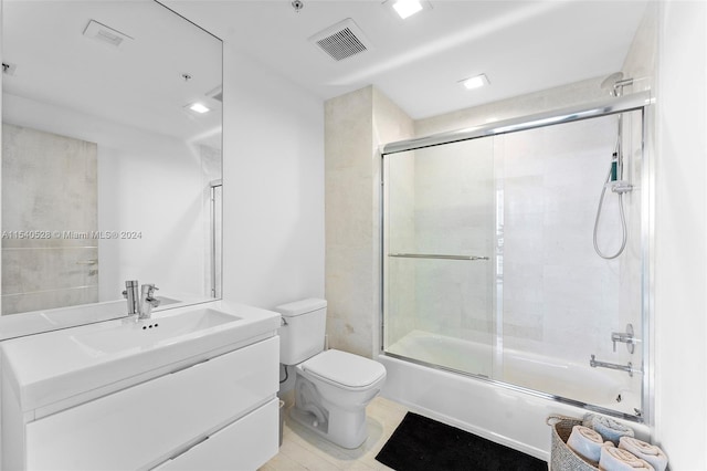 full bathroom with toilet, vanity with extensive cabinet space, tile floors, and bath / shower combo with glass door