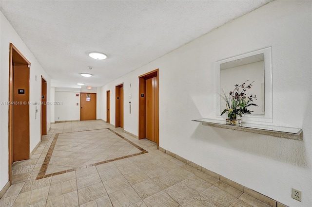 corridor featuring a textured ceiling, light tile floors, and elevator