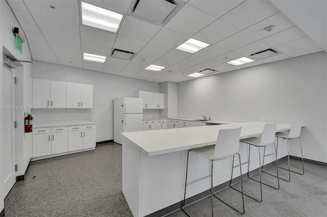 kitchen featuring a kitchen breakfast bar, white refrigerator, a paneled ceiling, white cabinets, and sink