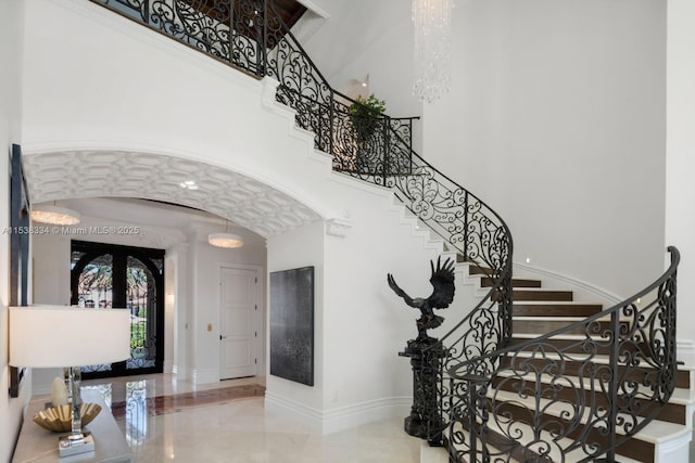 foyer entrance with a towering ceiling, arched walkways, baseboards, and stairway