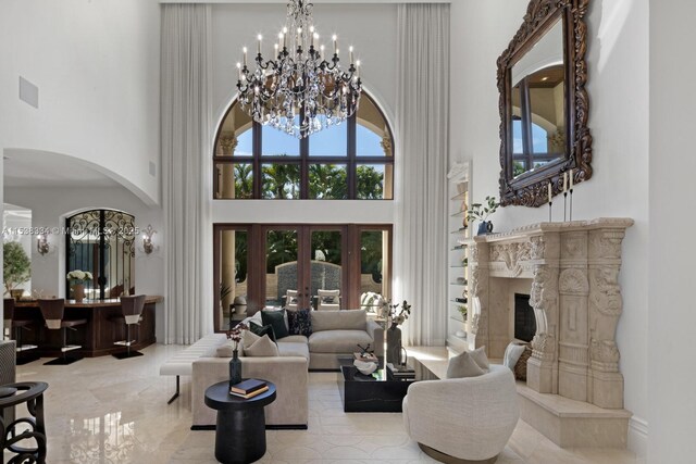living room with arched walkways, a towering ceiling, a high end fireplace, and a notable chandelier