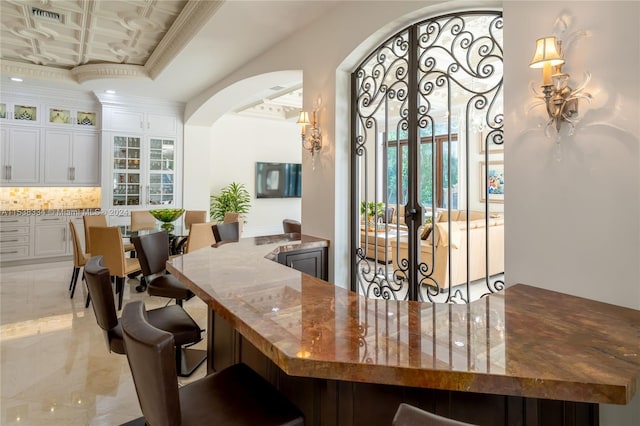 bar with coffered ceiling, ornamental molding, tasteful backsplash, a healthy amount of sunlight, and white cabinetry