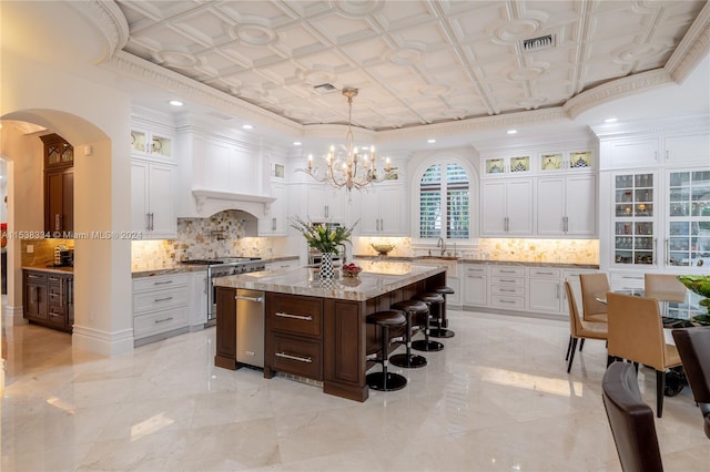 kitchen with light stone countertops, white cabinetry, hanging light fixtures, stainless steel gas range, and a kitchen island