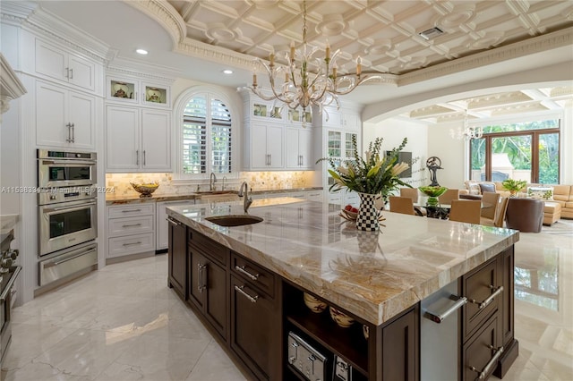 kitchen featuring dark brown cabinetry, a center island with sink, white cabinetry, and hanging light fixtures