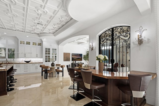 bar featuring decorative backsplash, marble finish floor, a raised ceiling, arched walkways, and visible vents