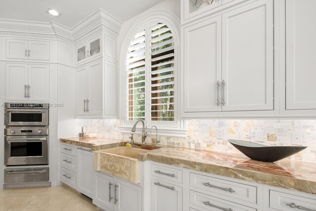 kitchen featuring a warming drawer, tasteful backsplash, double oven, a sink, and light stone countertops