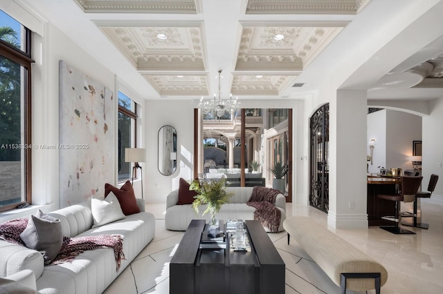 living room featuring baseboards, a chandelier, coffered ceiling, and crown molding