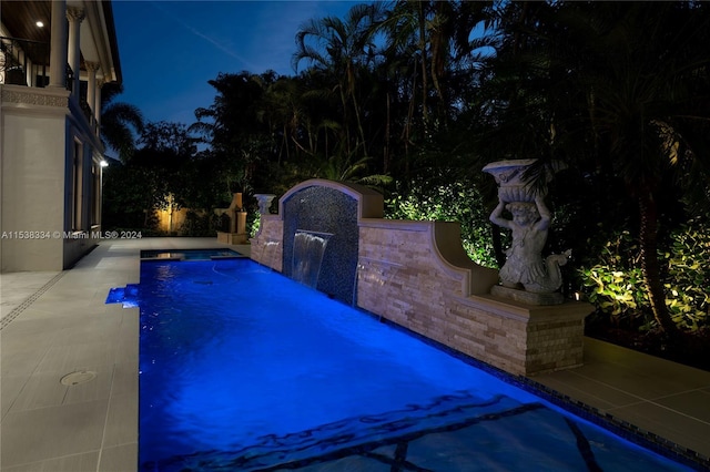 pool at night featuring pool water feature