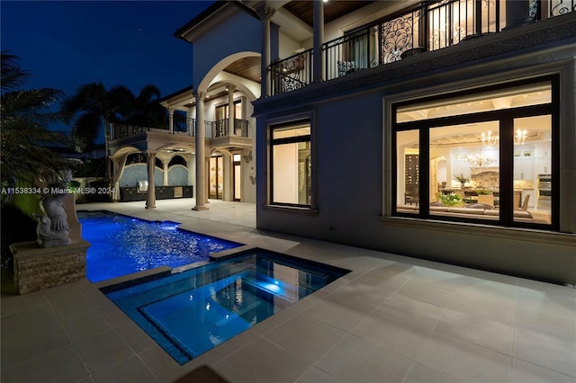 pool at night with an in ground hot tub and a patio