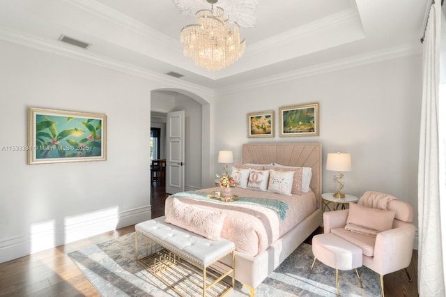 bedroom with a tray ceiling, wood finished floors, visible vents, arched walkways, and an inviting chandelier