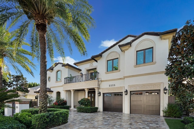 mediterranean / spanish-style home featuring driveway, a tile roof, stucco siding, an attached garage, and a balcony