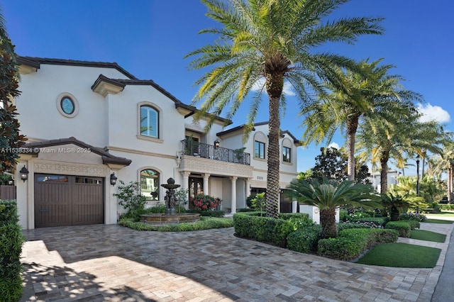 mediterranean / spanish-style home featuring a garage, a balcony, decorative driveway, and stucco siding