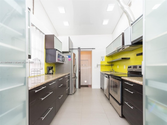 kitchen with backsplash, a barn door, light tile patterned floors, white cabinetry, and stainless steel appliances