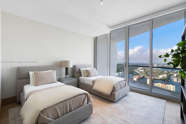 bedroom with access to exterior, floor to ceiling windows, a water view, and light wood-type flooring