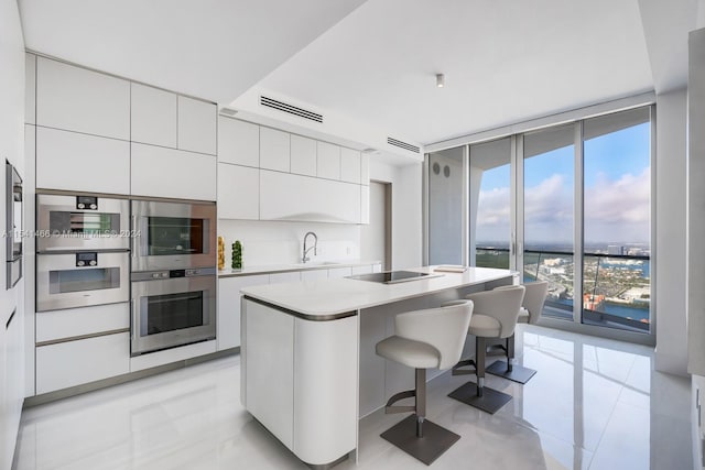 kitchen featuring double oven, a kitchen bar, light tile floors, white cabinets, and a kitchen island