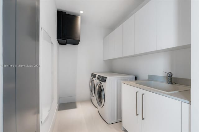 clothes washing area with washer and dryer, light hardwood / wood-style floors, cabinets, and sink