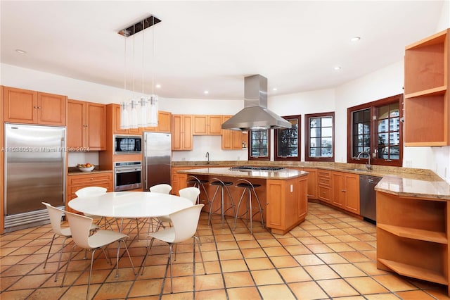 kitchen with pendant lighting, a center island, a breakfast bar area, built in appliances, and island exhaust hood