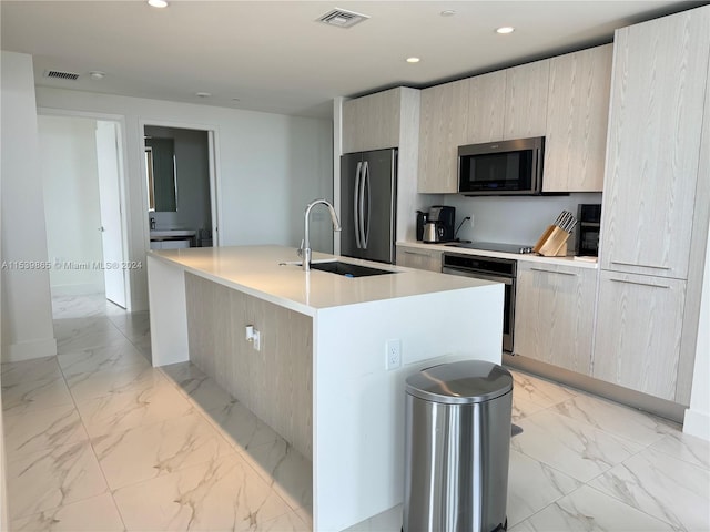 kitchen featuring light tile floors, stainless steel appliances, sink, and an island with sink