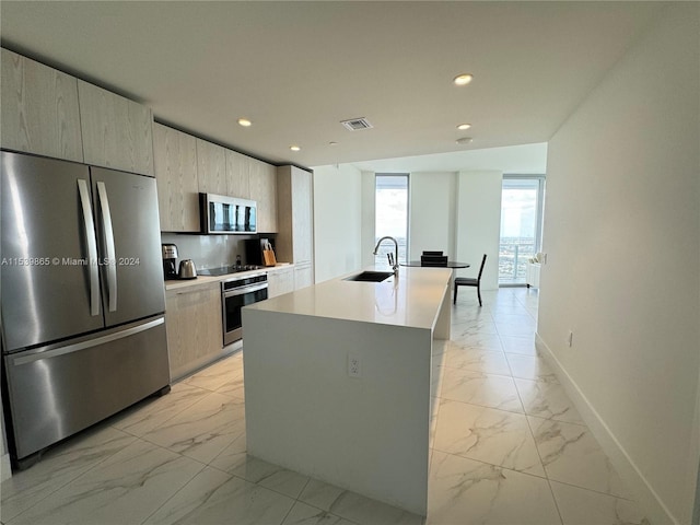 kitchen with light brown cabinets, tasteful backsplash, a center island with sink, appliances with stainless steel finishes, and sink