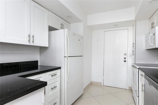 kitchen featuring white appliances, light tile flooring, white cabinetry, and dark stone countertops