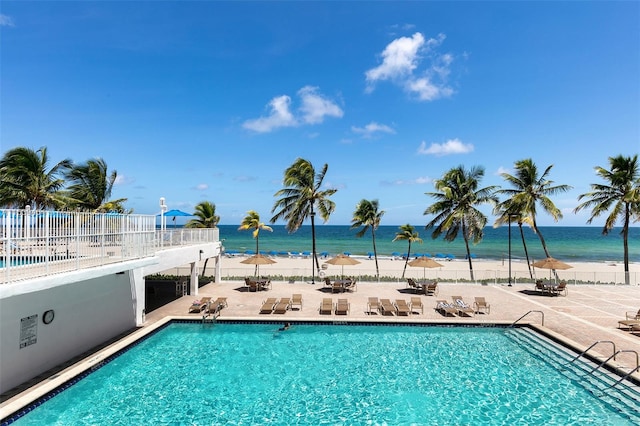 view of pool featuring a water view, a view of the beach, and a patio