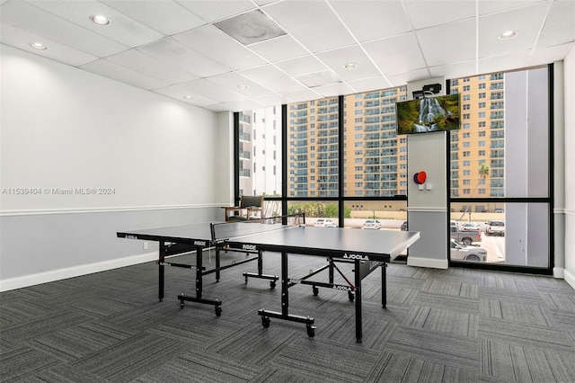 rec room with floor to ceiling windows, a drop ceiling, and dark carpet