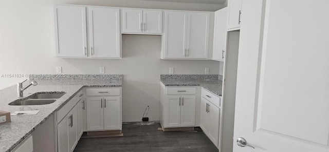 kitchen with a sink, light stone countertops, white cabinets, and dark wood finished floors